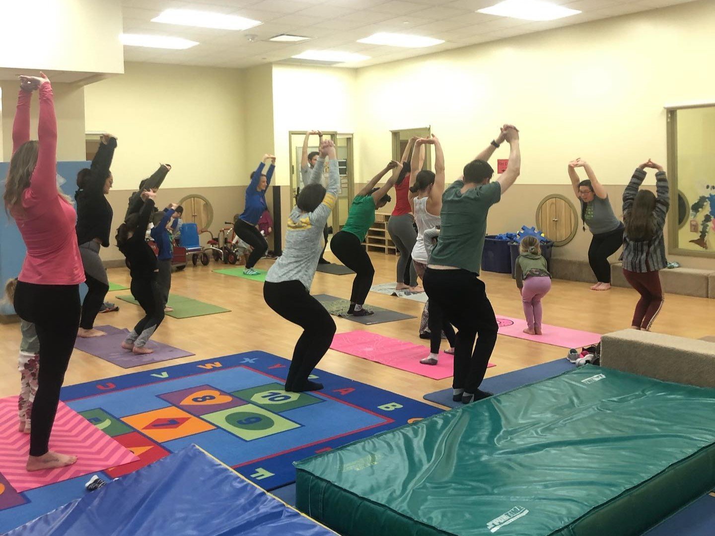 Students and their children balance in a sitting yoga pose with their hands above their heads